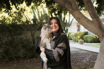 Alexis Tostado holds a gray and white cat and smiles.