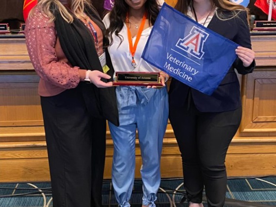 Three veterinary students hold a plaque and flag at a SAVMA event.