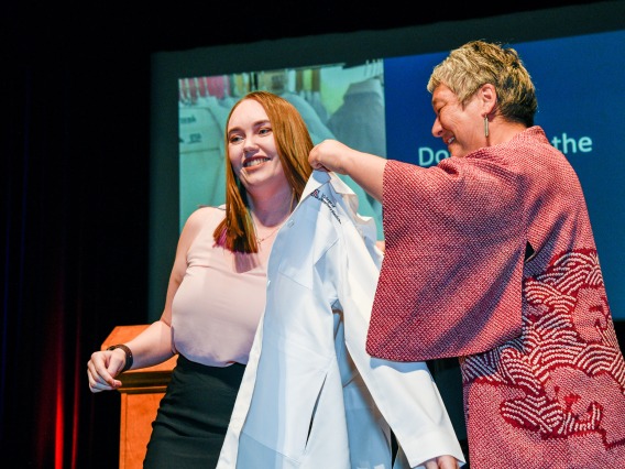 A student at the Class of 2023 White Coat ceremony is coated by her mentor.