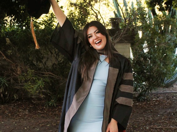 Alexis Tostado wears graduation regalia and holds her cap in the air.