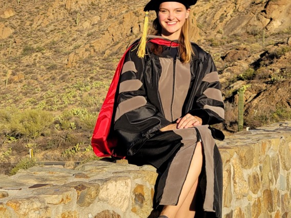 Atessa Szeglin wears graduation regalia and poses in front of a Tucson mountain landscape.