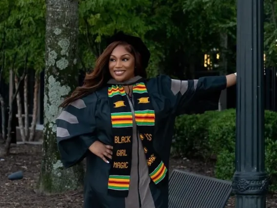 Brittany Johnson wears graduation regalia and poses in a park.