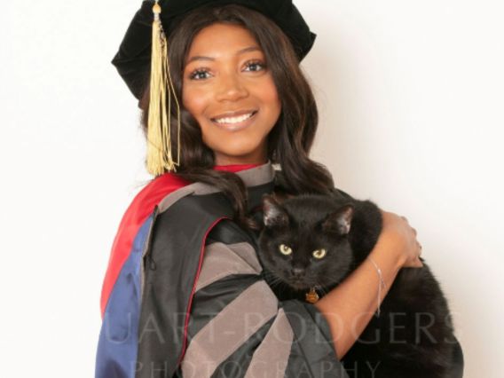 Deianira Smith wears graduation regalia and holds a black cat.