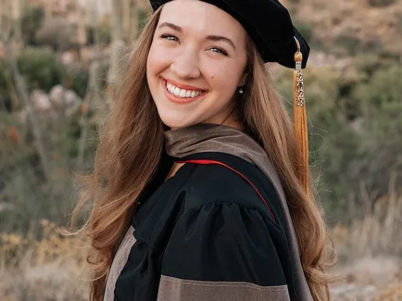 Morgan Beckham stands outdoors in front of a Tucson landscape and wears graduation regalia.