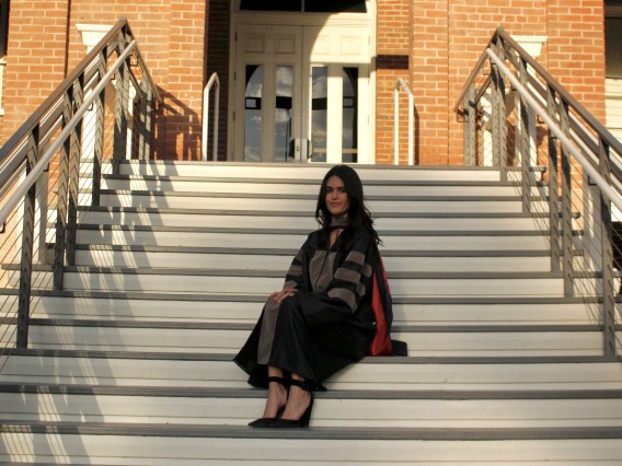 Shannon Khodadad wears graduation regalia and sits on the steps of a University of Arizona building.
