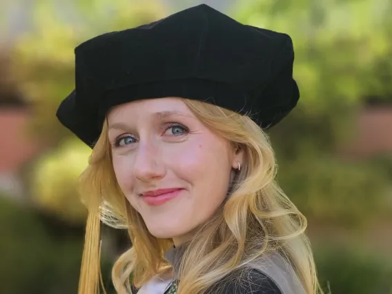 A woman wears black and gray doctoral regalia and smiles.