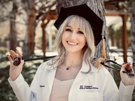 A woman wears a doctor's coat and doctoral tam and smiles.
