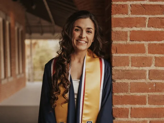 Woman with hair down in graduation regalia smiling.