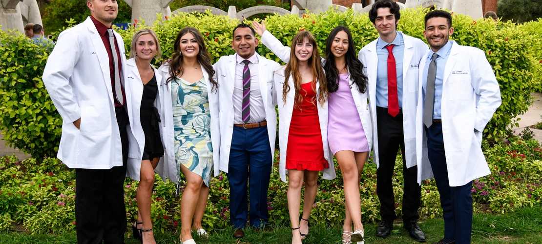 A group of students in white coats poses as a group outdoors.