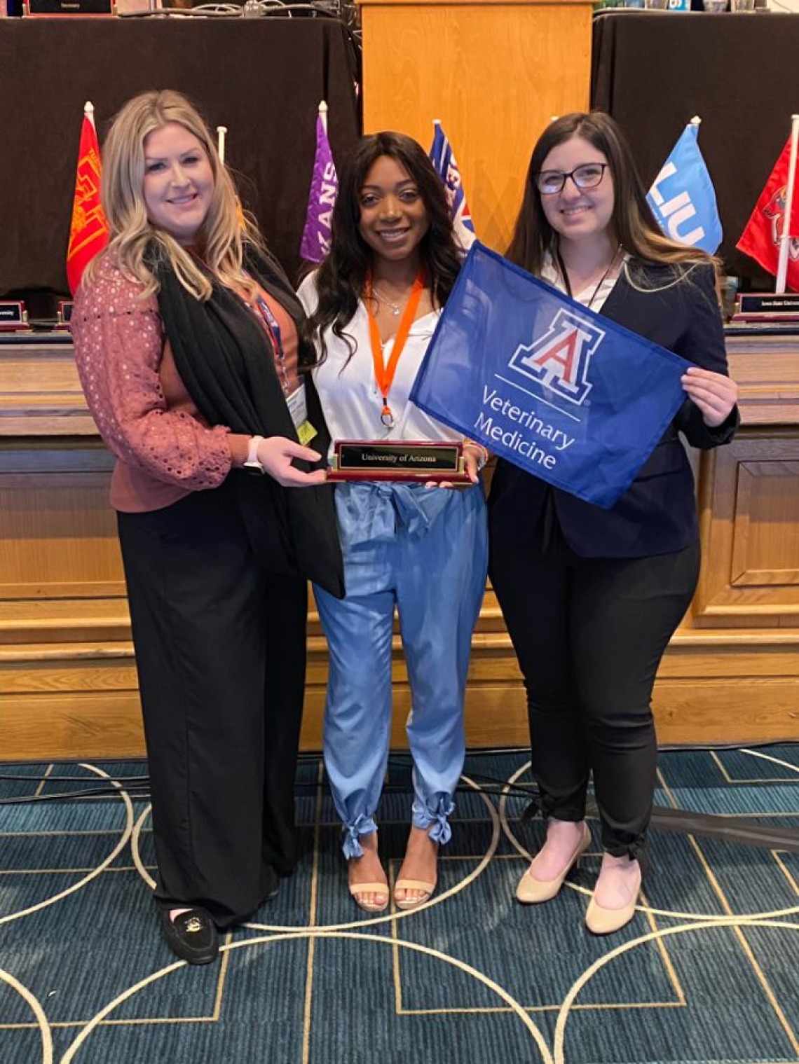 Three veterinary students hold a plaque and flag at a SAVMA event.