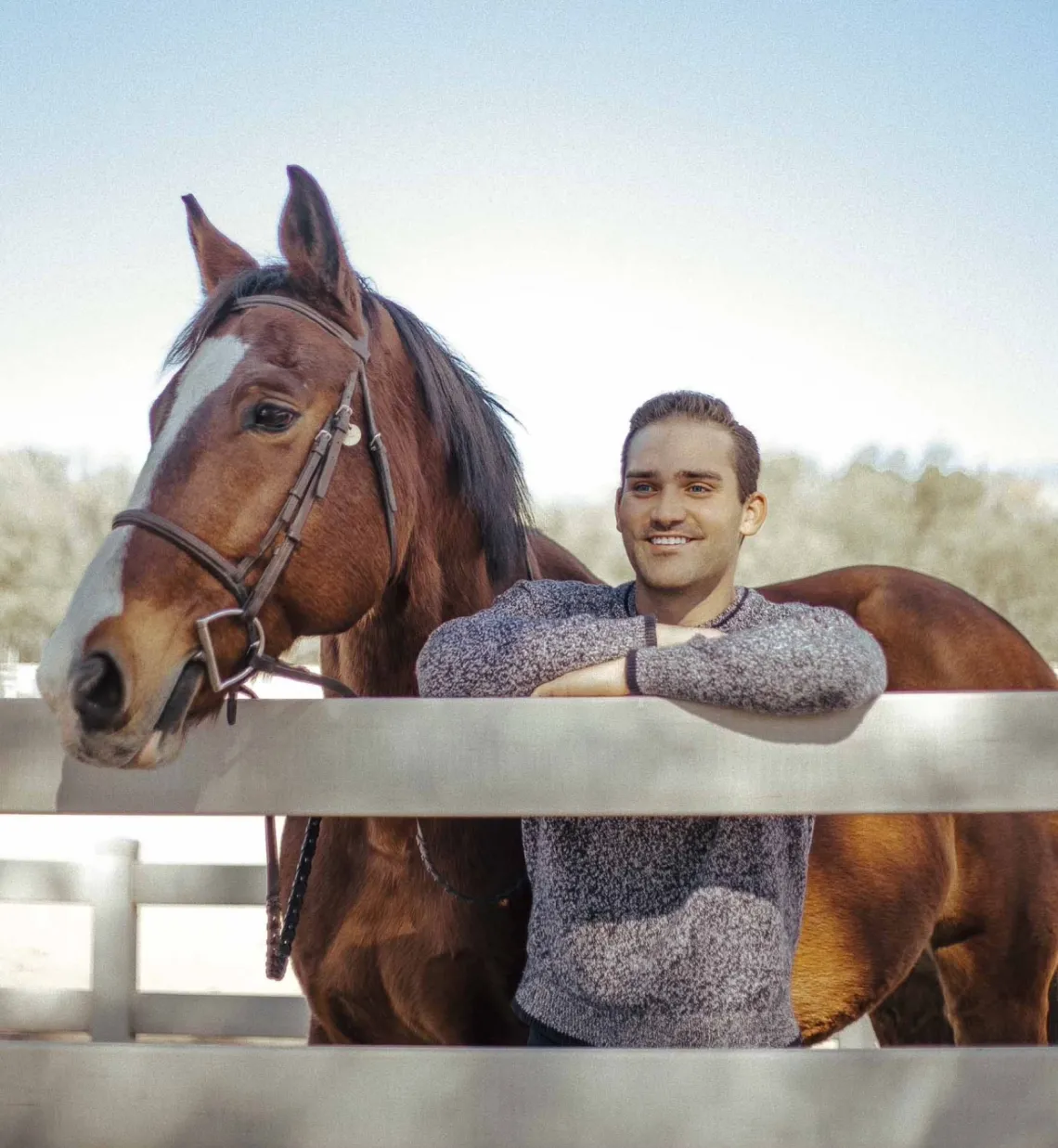 Student Justin Smith stands next to a white fence with a brown horse.