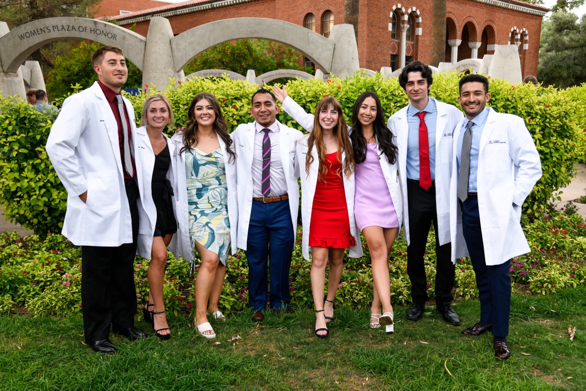 A group of students in white coats poses as a group outdoors.