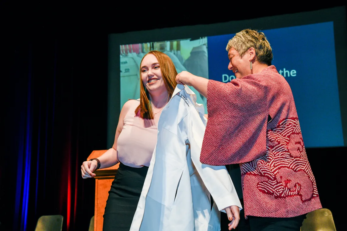 A student at the Class of 2023 White Coat ceremony is coated by her mentor.