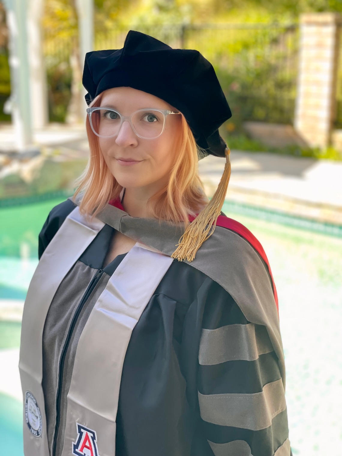 Ashley Sujata stands in front of a water feature and wears veterinary graduation regalia.