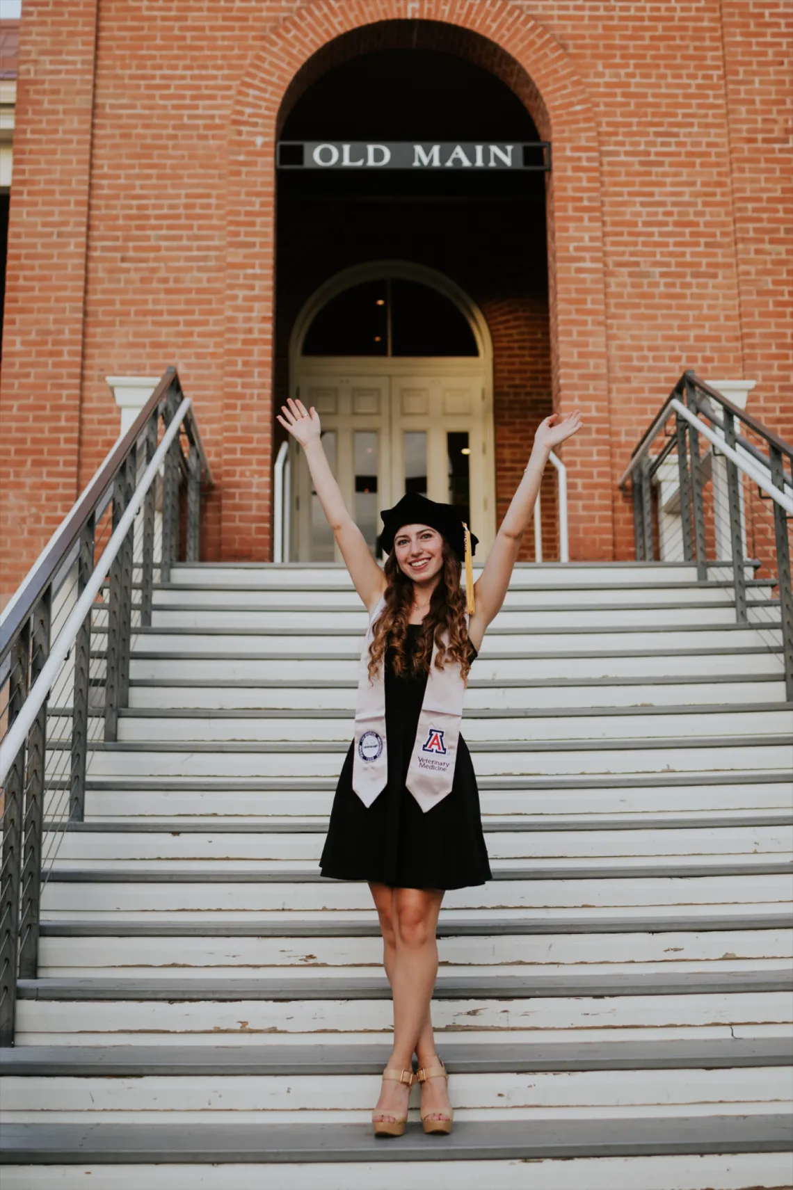 Adina Bronshtein stands in front of the Old Main building with her arms up in the air in celebration.