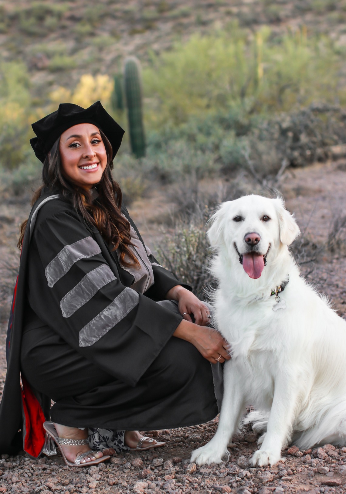 Camila Rocha wears graduation regalia and poses with a light-colored dog.