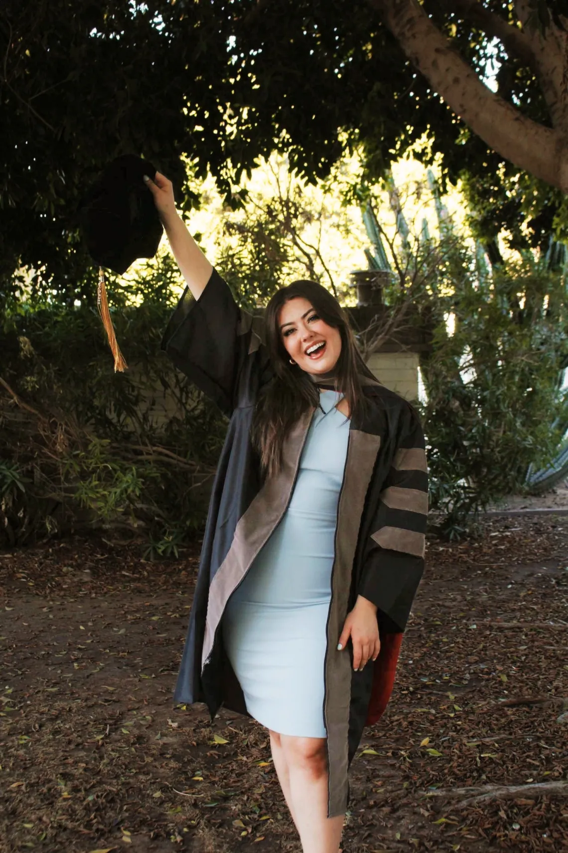 Alexis Tostado wears graduation regalia and holds her cap in the air.