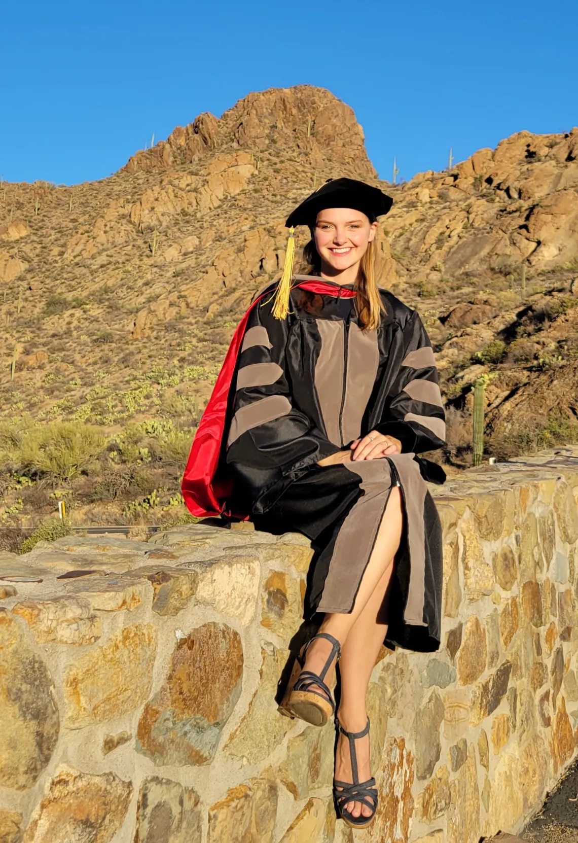 Atessa Szeglin wears graduation regalia and poses in front of a Tucson mountain landscape.