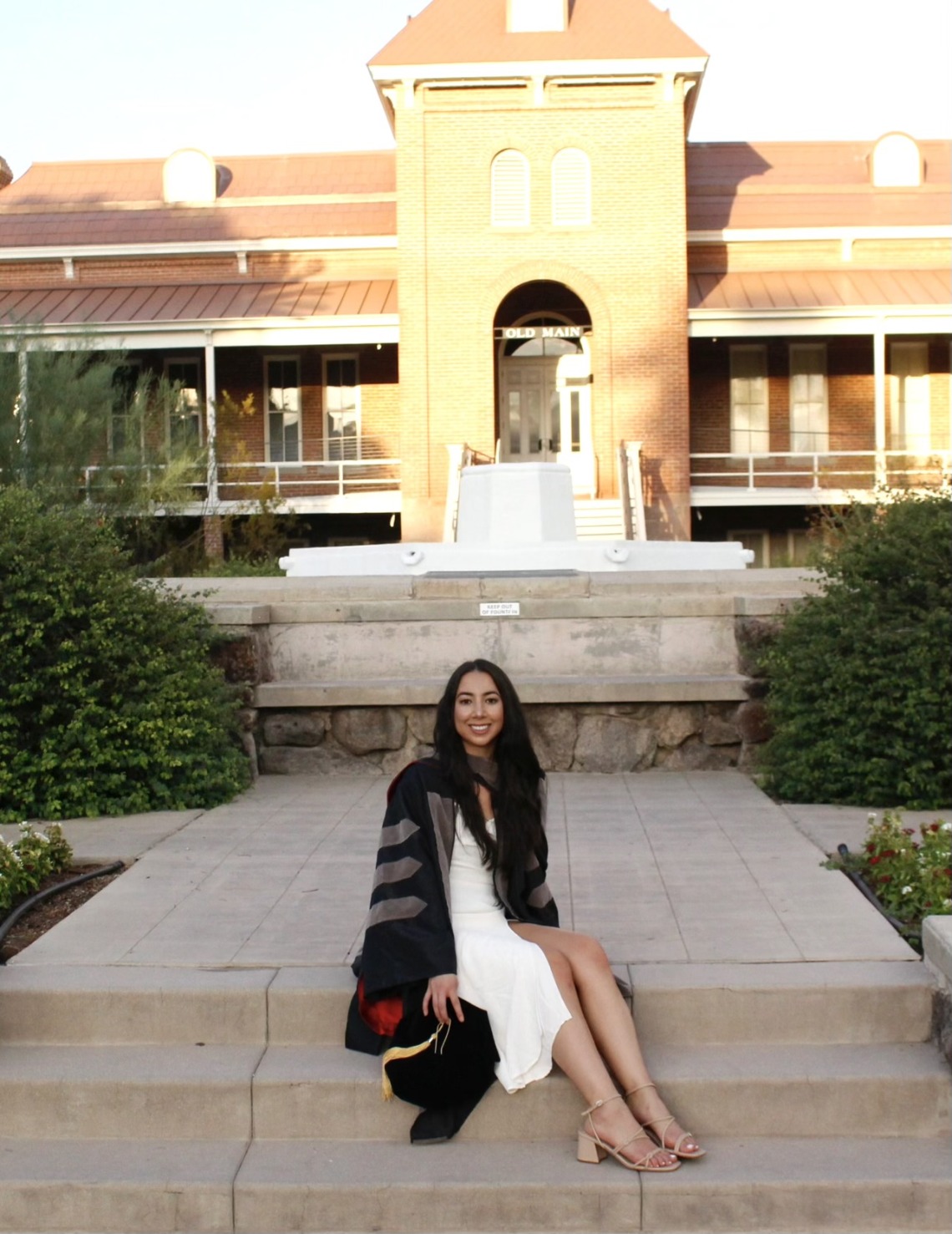 Catherine Wu wears graduation regalia and poses in front of a University of Arizona building.