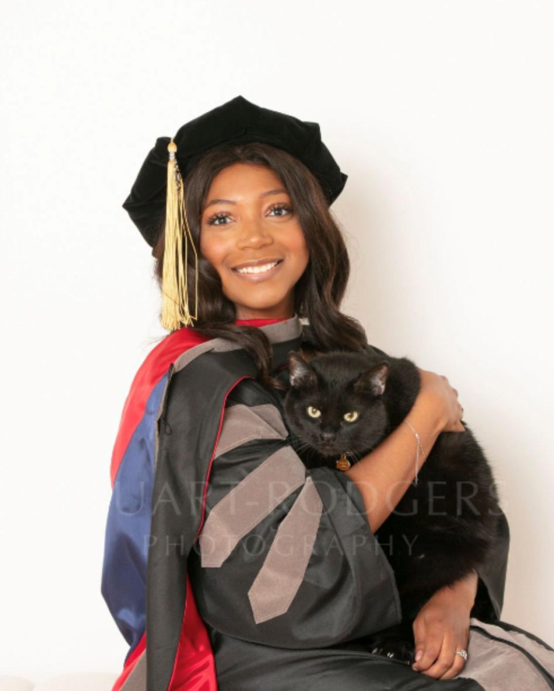 Deianira Smith wears graduation regalia and holds a black cat.