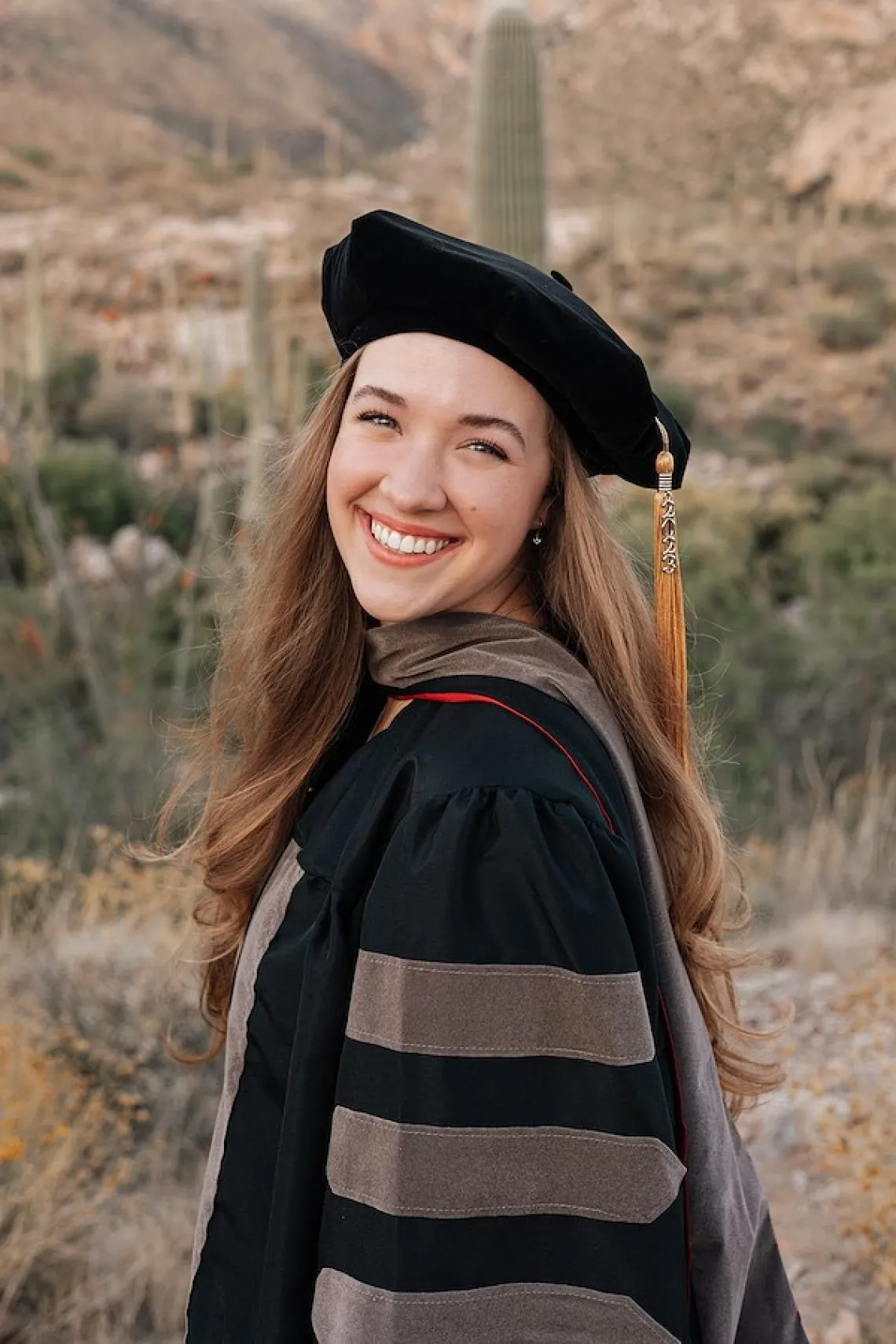 Morgan Beckham stands outdoors in front of a Tucson landscape and wears graduation regalia.