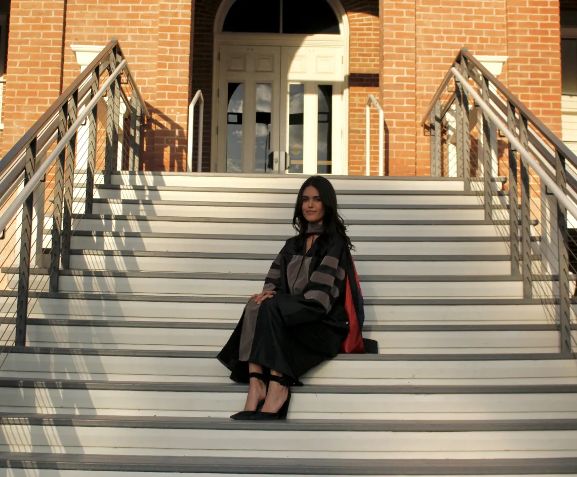 Shannon Khodadad wears graduation regalia and sits on the steps of a University of Arizona building.