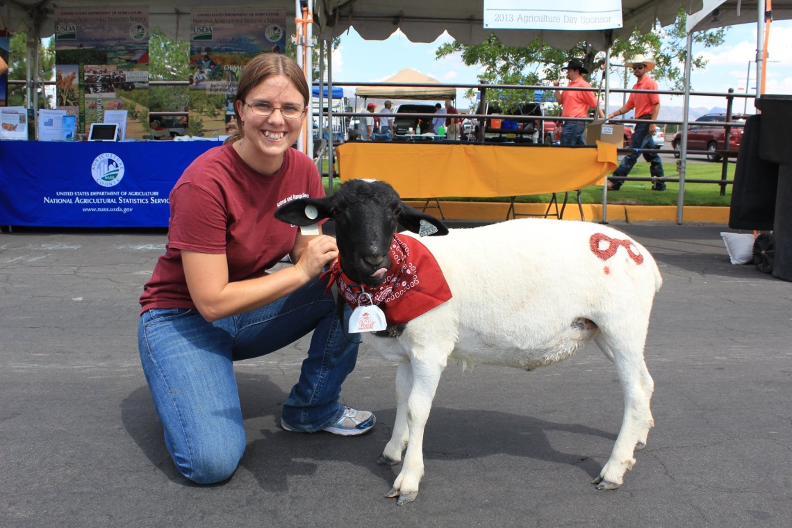 Professor Megan Owen poses with a small sheep with a white body and black head.