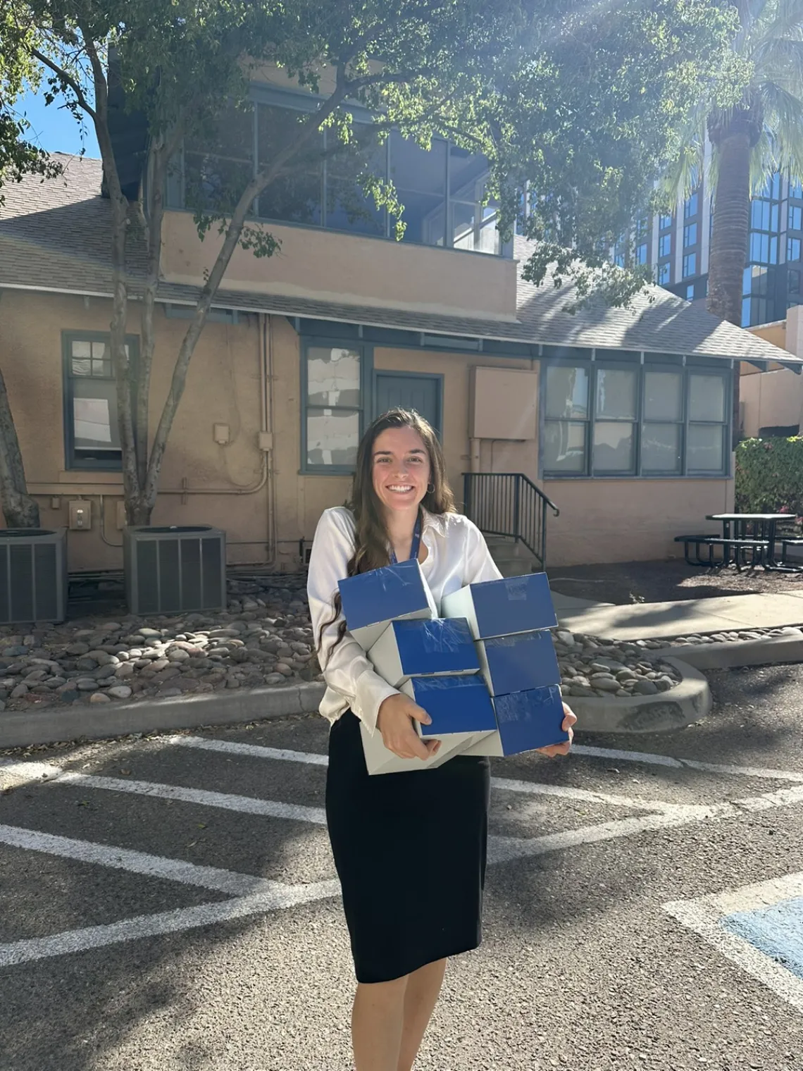 A woman stands in front of the Human-Animal Interaction research house and holds an armload of test kits in blue boxes.