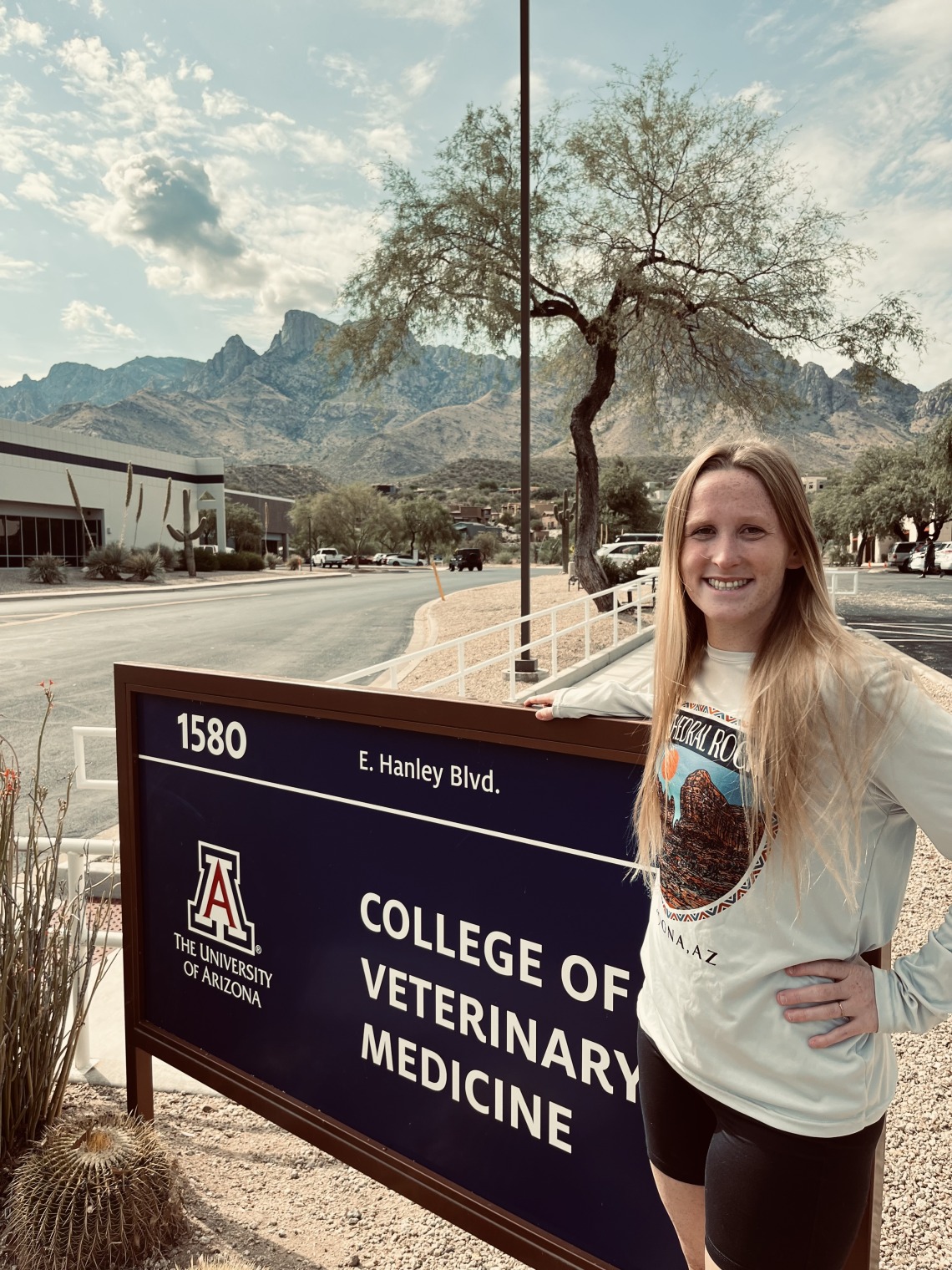 Katherine Liccione poses in front of the "College of Veterinary Medicine" sign, against an overcast mountain background.
