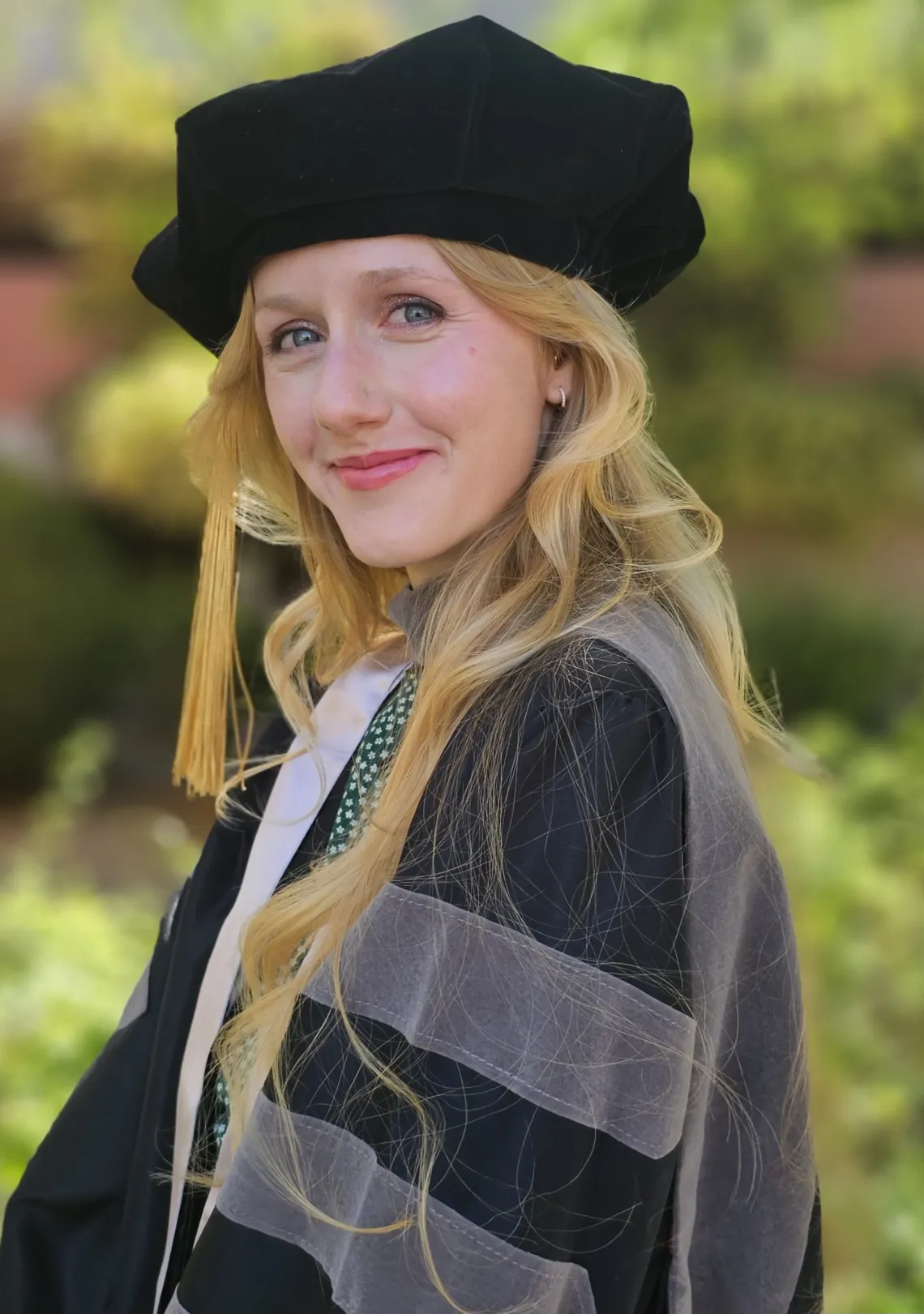 A woman wears black and gray doctoral regalia and smiles.