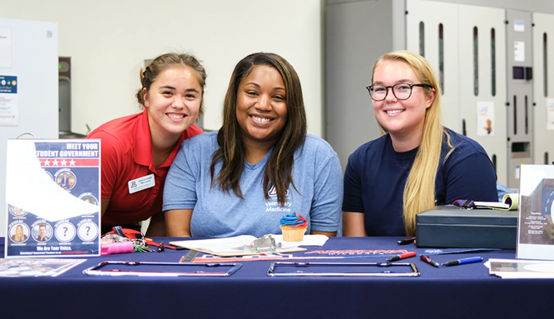 Three students sit at table during club fair
