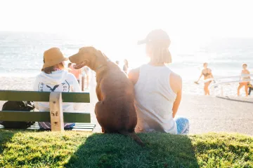 A woman sits next to a dog outdoors.