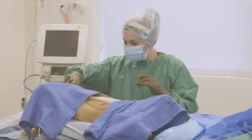 A veterinary student in scrubs and gloves participates in a surgical simulation, operating on a dog mannikin.