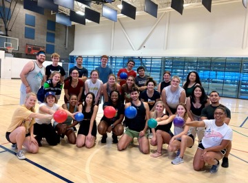 A group of over 25 students stand together in a basketball court. Some are holding dodgeballs.