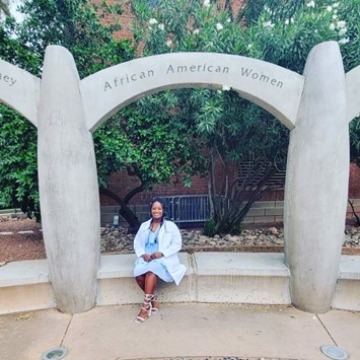 Arianna Adams sits under an arch that reads "African American Women" in the Women's Plaza of Honor at the University of Arizona.