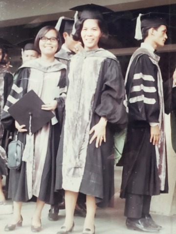 A woman, smiling, wears graduation regalia.