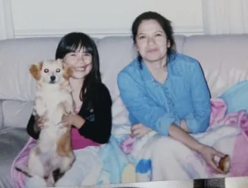 A young girl sits next to her mother and holds a small dog.