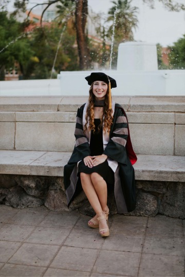 Adina Bronshtein wears graduation regalia and poses in front of a fountain.