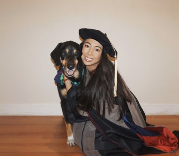 Catherine Wu wears graduation regalia and poses next to a black and tan dog.