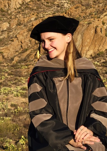 Atessa Szeglin wears graduation regalia and poses in front of a Tucson mountain landscape.