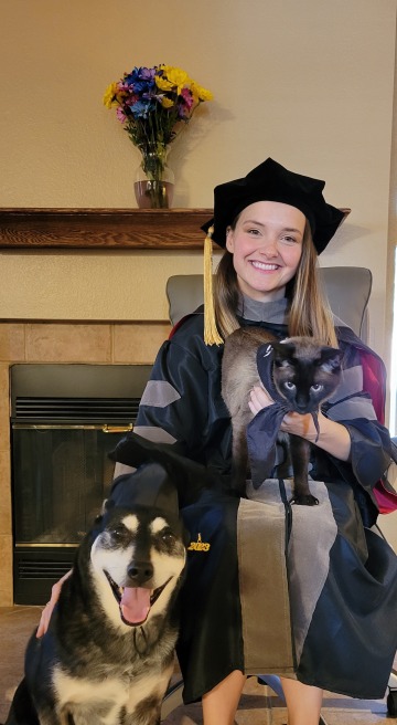 Atessa Szeglin wears graduation regalia and sits indoors with a dog and a cat.