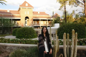 Catherine Wu wears graduation regalia and poses in front of a University of Arizona building.