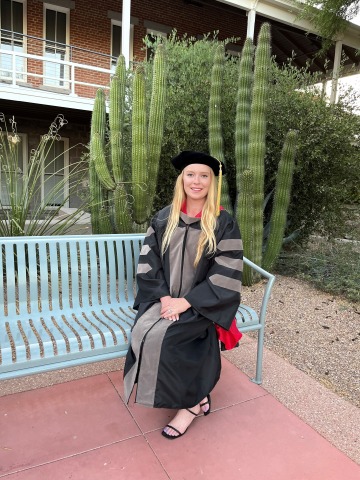 Caylee Childress wears graduation regalia and poses on a bench on the University of Arizona campus.
