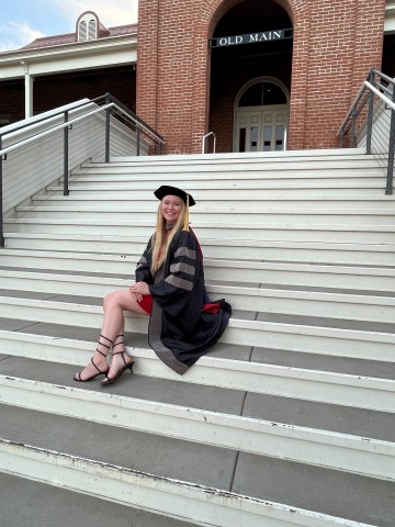 Caylee Childress wears graduation regalia and poses on the stairs outside Old Main.