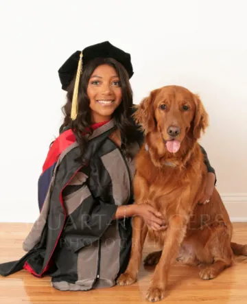 Deianira Smith wears graduation regalia and poses with a Golden Retriever.