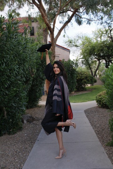 Shannon Khodadad wears graduation regalia and holds her cap up in the air.
