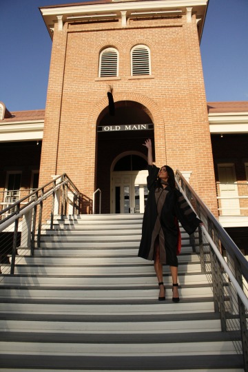 Shannon Khodadad wears graduation regalia and stands on the steps outside a University of Arizona building.