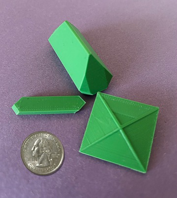 Three sample 3D-printed crystals, alongside a quarter for scale. They are about twice the size of the quarter.