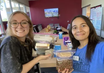 Two club members smile and hold up plastic bags filled with food.