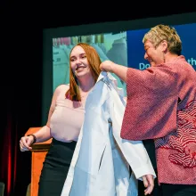 A student at the Class of 2023 White Coat ceremony is coated by her mentor.